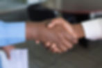 Two men shaking hands in a business setting. This photo focuses on their hands. 